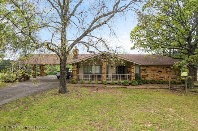 single story home featuring a chimney, a porch, driveway, stone siding, and a front yard