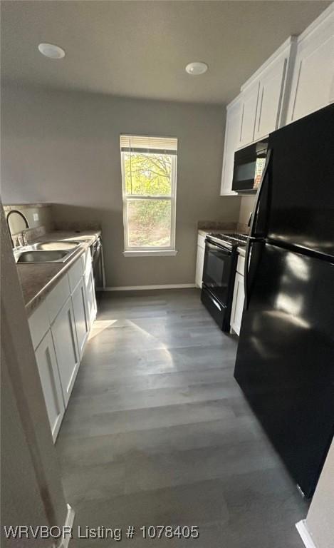 kitchen with black appliances, white cabinets, wood-type flooring, and sink