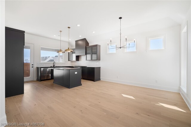 kitchen with tasteful backsplash, custom exhaust hood, decorative light fixtures, light hardwood / wood-style flooring, and a center island