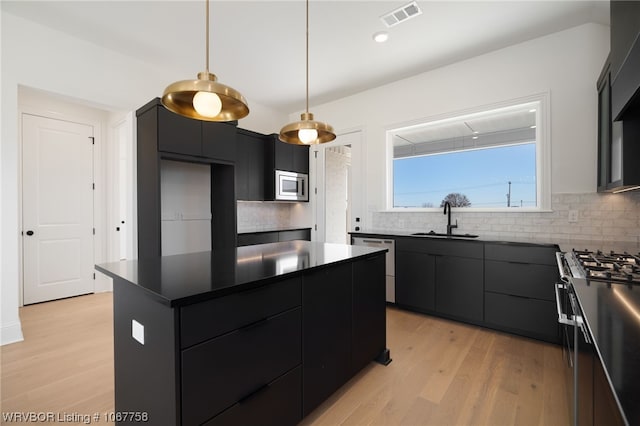 kitchen with sink, a center island, stainless steel appliances, light hardwood / wood-style floors, and decorative light fixtures