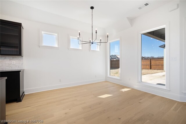 unfurnished dining area with plenty of natural light, a chandelier, and light hardwood / wood-style floors