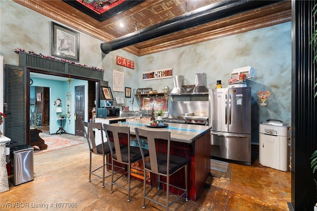 kitchen featuring stainless steel refrigerator, crown molding, extractor fan, concrete flooring, and a breakfast bar area