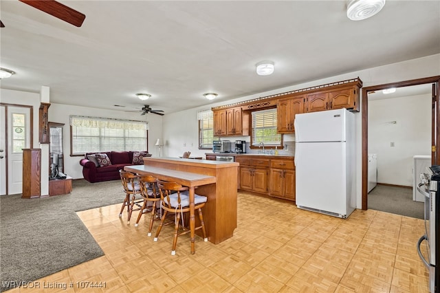 kitchen with sink, white refrigerator, light colored carpet, a breakfast bar area, and a kitchen island