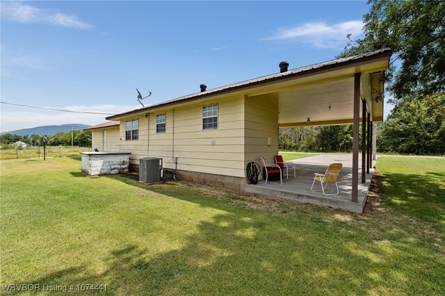 back of property featuring a mountain view, central AC, a patio area, and a lawn