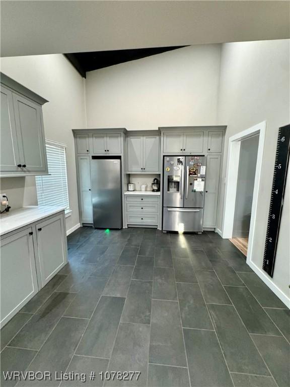 kitchen featuring stainless steel refrigerator, stainless steel fridge with ice dispenser, gray cabinets, and a high ceiling