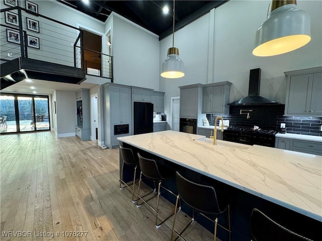 kitchen featuring wall chimney exhaust hood, a high ceiling, tasteful backsplash, a breakfast bar area, and gray cabinets