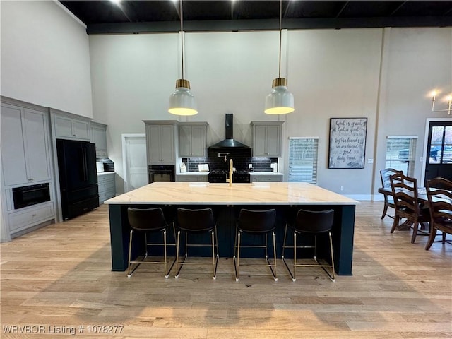 kitchen featuring light stone countertops, wall chimney range hood, backsplash, gray cabinets, and black appliances