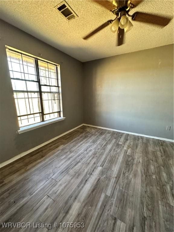 spare room with dark wood-type flooring, a healthy amount of sunlight, and a textured ceiling