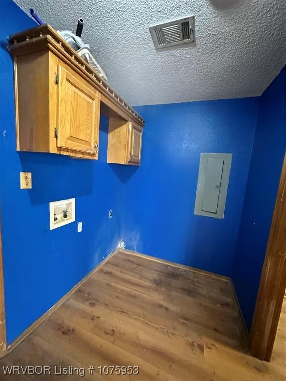 laundry area with cabinets, washer hookup, electric panel, light hardwood / wood-style floors, and a textured ceiling