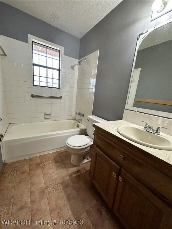 full bathroom featuring tiled shower / bath, vanity, a textured ceiling, and toilet