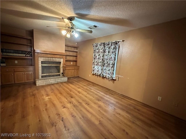 unfurnished living room with ceiling fan, a brick fireplace, a textured ceiling, and light hardwood / wood-style flooring