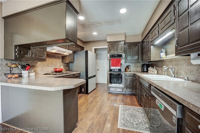 kitchen with sink, stainless steel appliances, backsplash, a textured ceiling, and light wood-type flooring