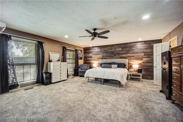 bedroom with carpet flooring, rustic walls, a textured ceiling, ceiling fan, and wood walls