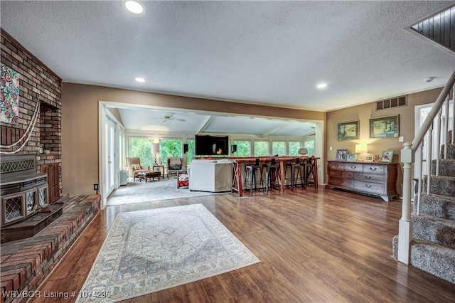 living room with ceiling fan, wood-type flooring, a textured ceiling, and brick wall