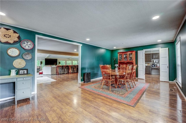 dining room featuring crown molding, wood-type flooring, and a textured ceiling