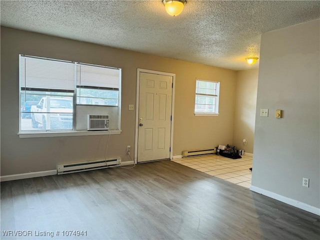 empty room with a textured ceiling, cooling unit, light hardwood / wood-style flooring, and a baseboard heating unit