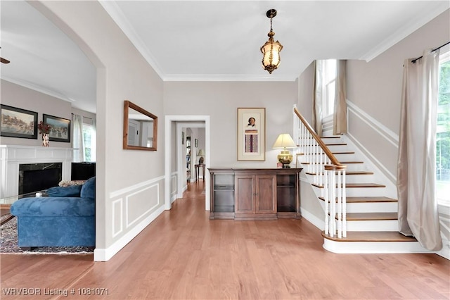 foyer entrance featuring healthy amount of natural light, light wood finished floors, stairway, crown molding, and a wainscoted wall