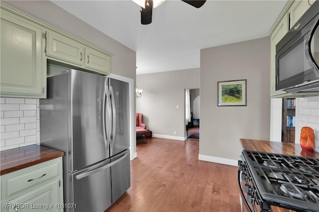 kitchen with freestanding refrigerator, black microwave, butcher block countertops, a ceiling fan, and tasteful backsplash
