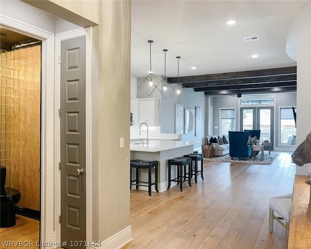 kitchen with white cabinetry, sink, french doors, a breakfast bar, and light wood-type flooring