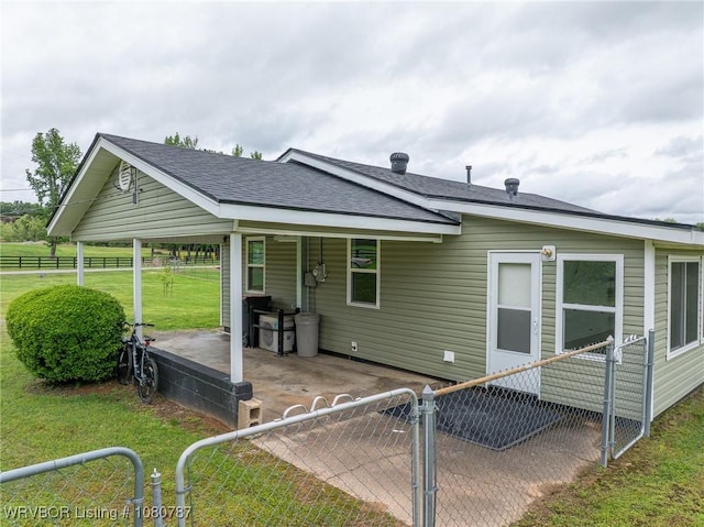 rear view of property with a lawn, a patio, fence private yard, roof with shingles, and a gate