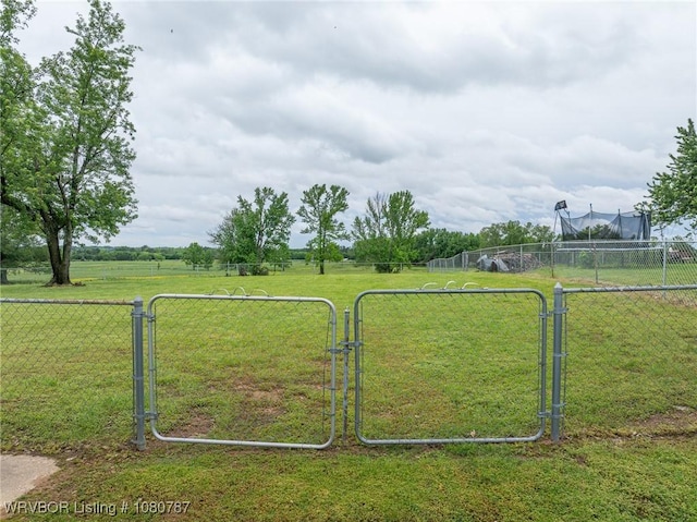 view of gate featuring fence, a rural view, and a lawn