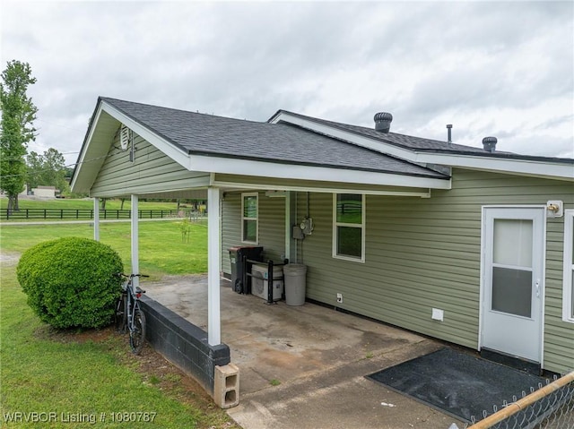 exterior space featuring a yard, fence, a patio area, a shingled roof, and an attached carport