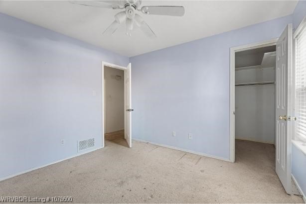 unfurnished bedroom with ceiling fan, a spacious closet, light carpet, and a closet