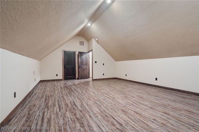 bonus room with lofted ceiling, wood finished floors, a textured ceiling, visible vents, and baseboards