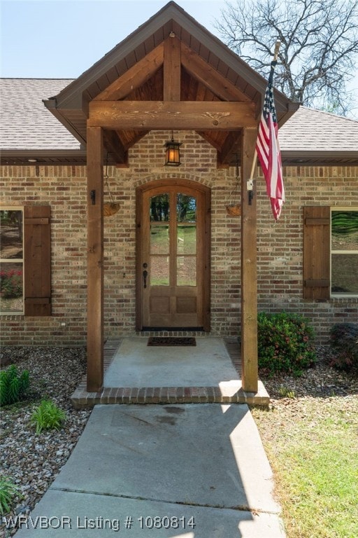 doorway to property featuring roof with shingles and brick siding