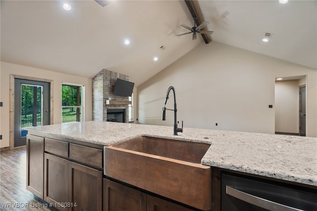 kitchen featuring a ceiling fan, dark brown cabinets, a sink, a brick fireplace, and vaulted ceiling with beams