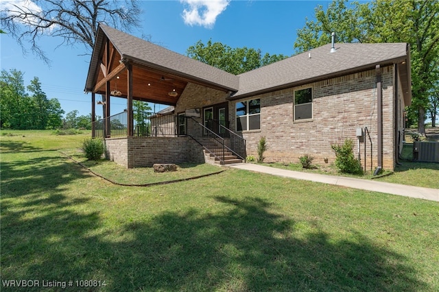 back of house featuring a yard, a shingled roof, central AC unit, and brick siding