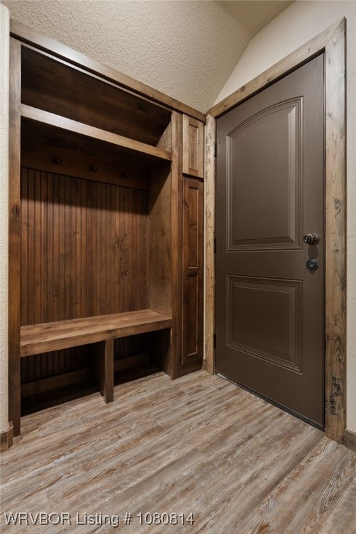 mudroom featuring light wood-style floors, lofted ceiling, and a textured ceiling
