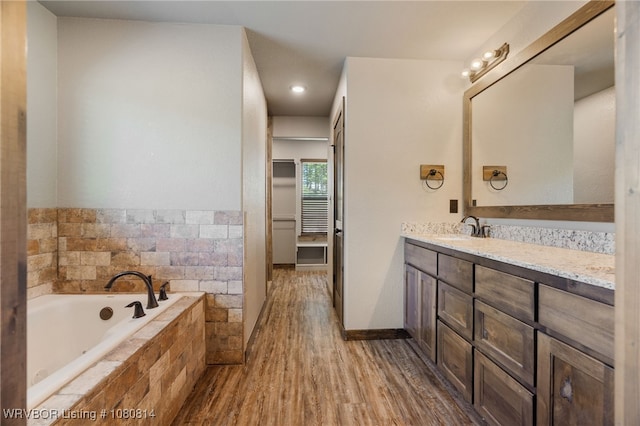 full bathroom with vanity, a spacious closet, a garden tub, and wood finished floors