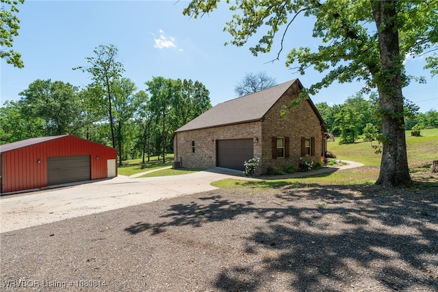 view of side of property with a detached garage, brick siding, and an outbuilding