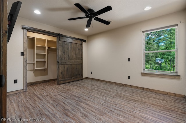 unfurnished bedroom with recessed lighting, a barn door, baseboards, and wood finished floors