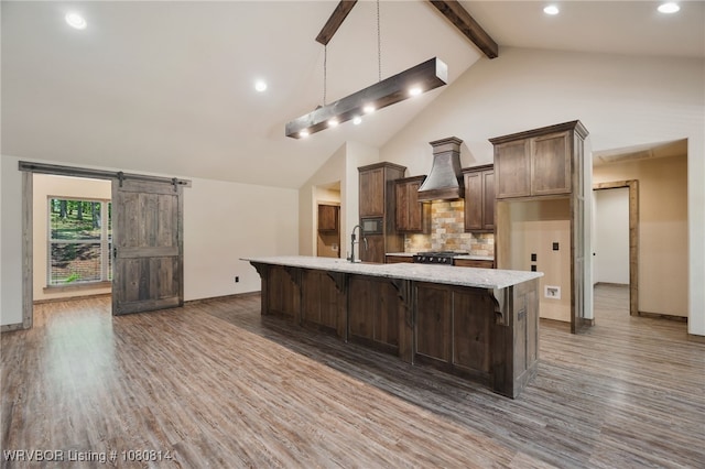 kitchen featuring a large island, wood finished floors, custom exhaust hood, decorative backsplash, and baseboards