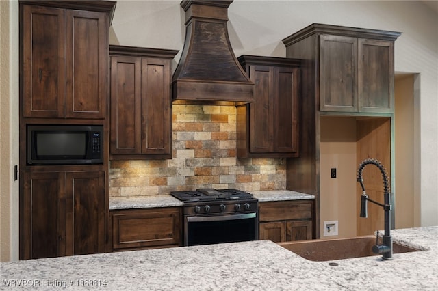 kitchen featuring black gas range oven, built in microwave, a sink, custom range hood, and backsplash