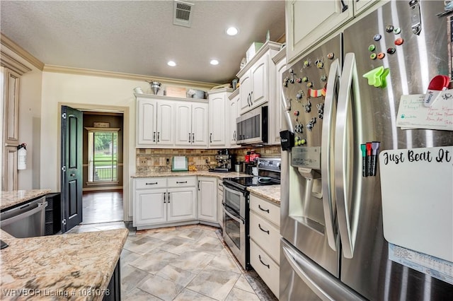 kitchen with appliances with stainless steel finishes, backsplash, light stone countertops, white cabinetry, and ornamental molding