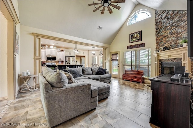 living room featuring ceiling fan, high vaulted ceiling, and a stone fireplace
