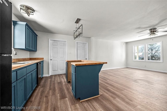 kitchen featuring blue cabinetry, butcher block counters, dark wood-style floors, and a sink