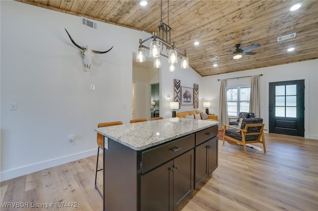 kitchen with a kitchen breakfast bar, light stone counters, wood ceiling, pendant lighting, and a center island