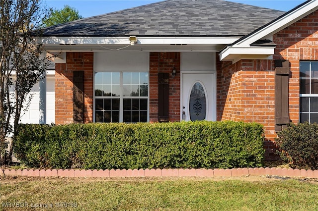 entrance to property with brick siding, a lawn, and roof with shingles