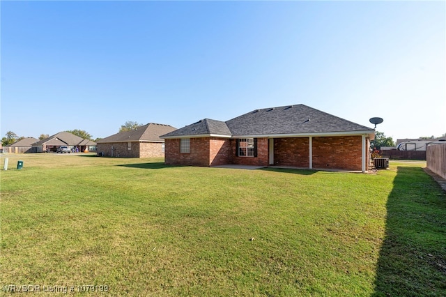 rear view of property featuring roof with shingles, brick siding, a lawn, central AC, and fence