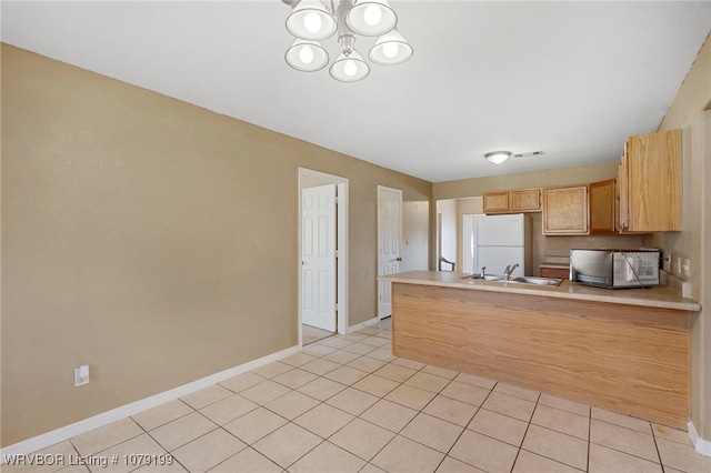 kitchen with light tile patterned floors, light brown cabinets, a peninsula, light countertops, and freestanding refrigerator