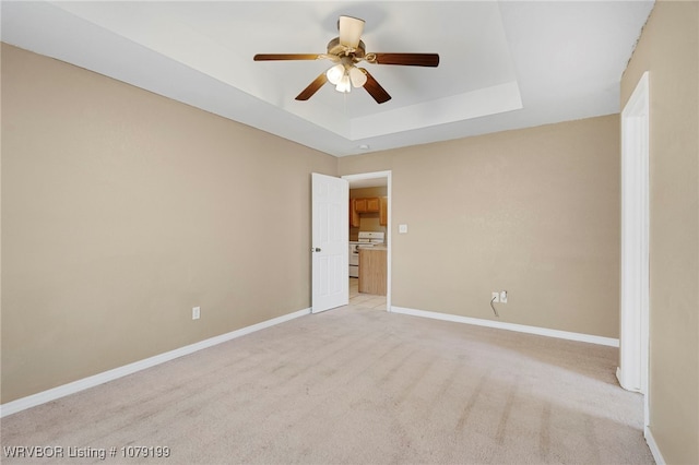 unfurnished room featuring a tray ceiling, light colored carpet, ceiling fan, and baseboards