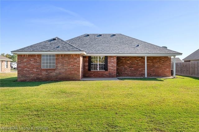 back of property featuring a yard, brick siding, a shingled roof, and fence