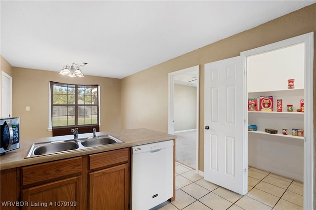 kitchen featuring white dishwasher, a sink, light countertops, brown cabinetry, and stainless steel microwave