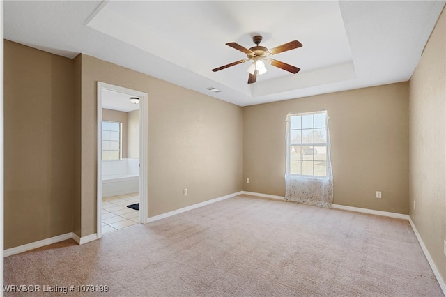 unfurnished room with baseboards, visible vents, a raised ceiling, a ceiling fan, and light colored carpet