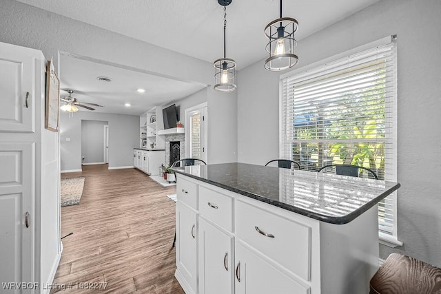 2509 Roxbury Ln, Fort Smith, AR 72908 - kitchen featuring a ceiling fan, light wood-type flooring, white cabinetry, a fireplace, and hanging light fixtures