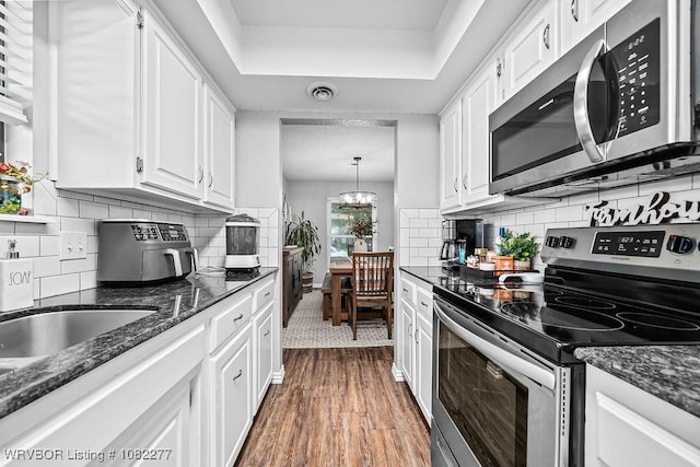 2509 Roxbury Ln, Fort Smith, AR 72908 - kitchen featuring appliances with stainless steel finishes, white cabinets, dark wood finished floors, a tray ceiling, and dark stone counters